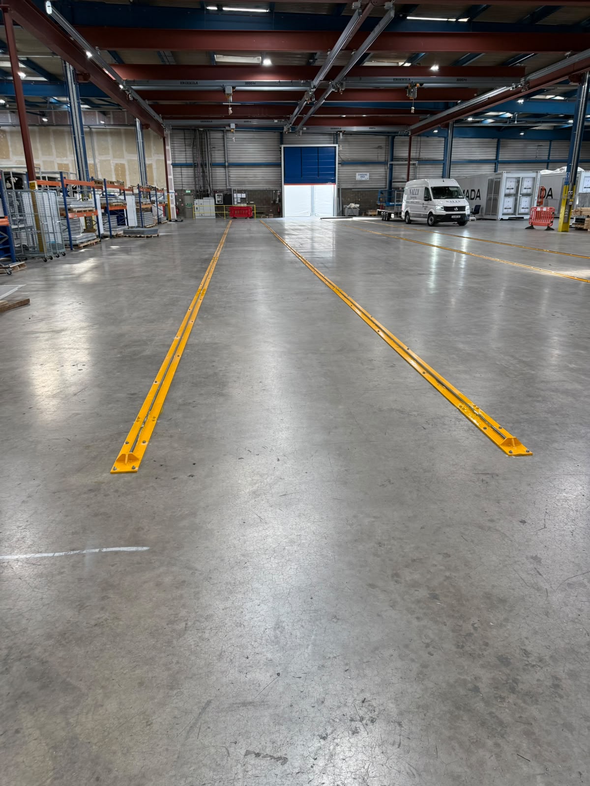 Long yellow painted steel guide rails bolted into a factory floor running towards a loading door