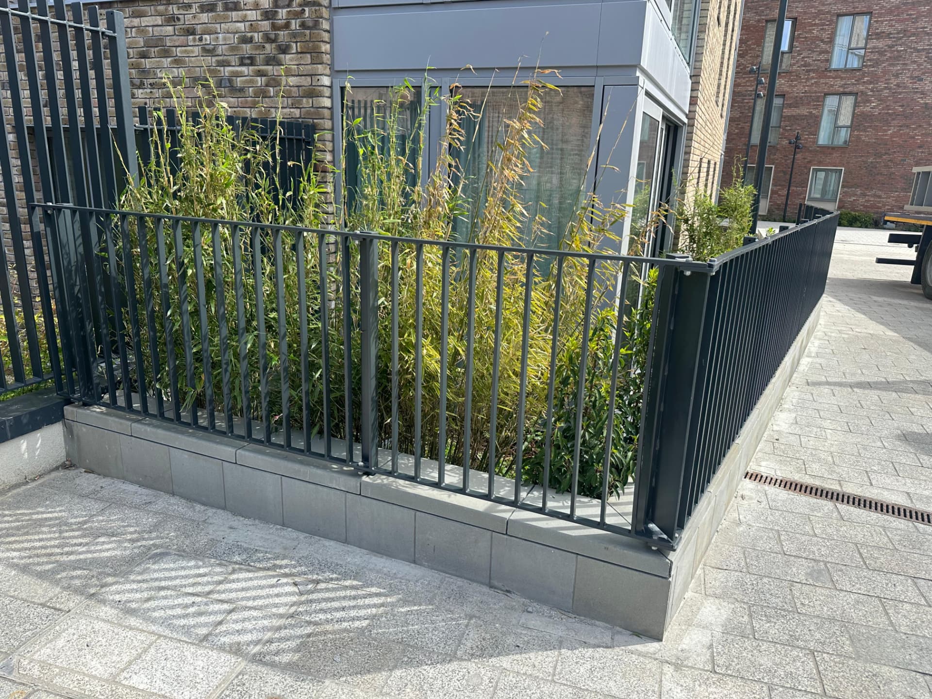 Run of dark grey railings enclosing a planting bed with corner posts and base plates