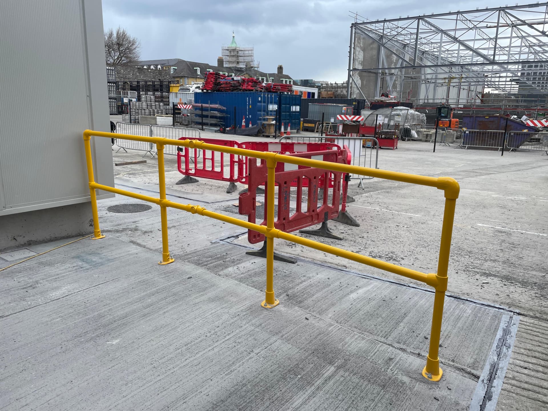Yellow tubular safety handrail on a concrete slab edge with a construction site behind