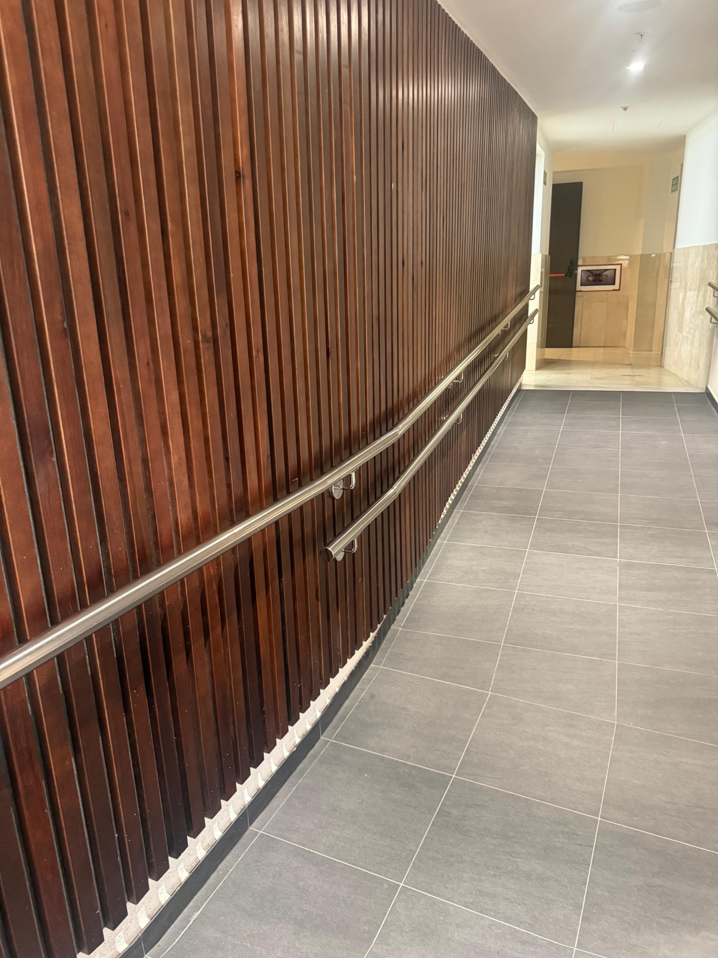 Stainless handrail run along a timber slatted corridor wall in a hotel