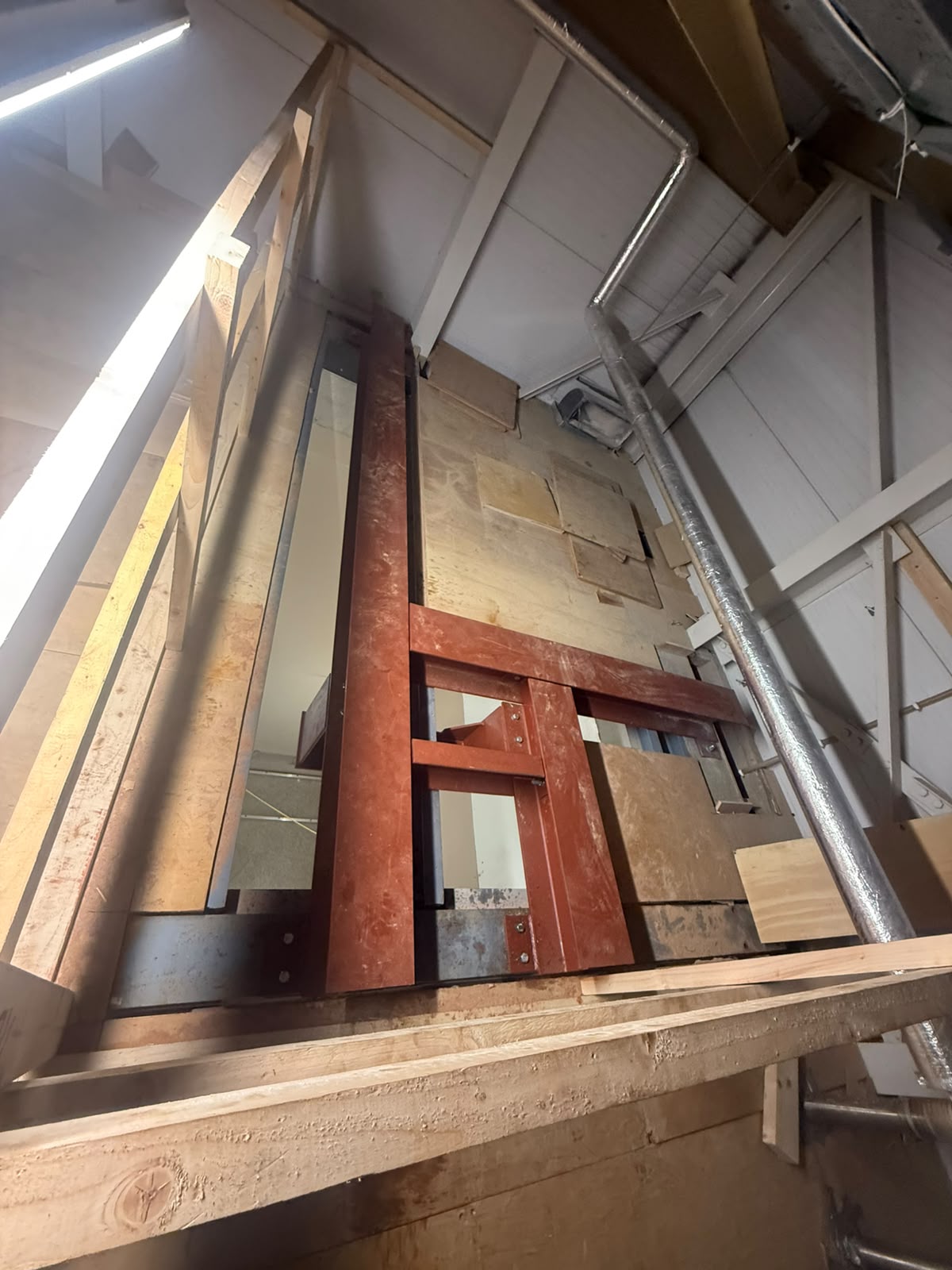 Red oxide welded steel lift shaft frame looking down through the temporary timber decking of the opening