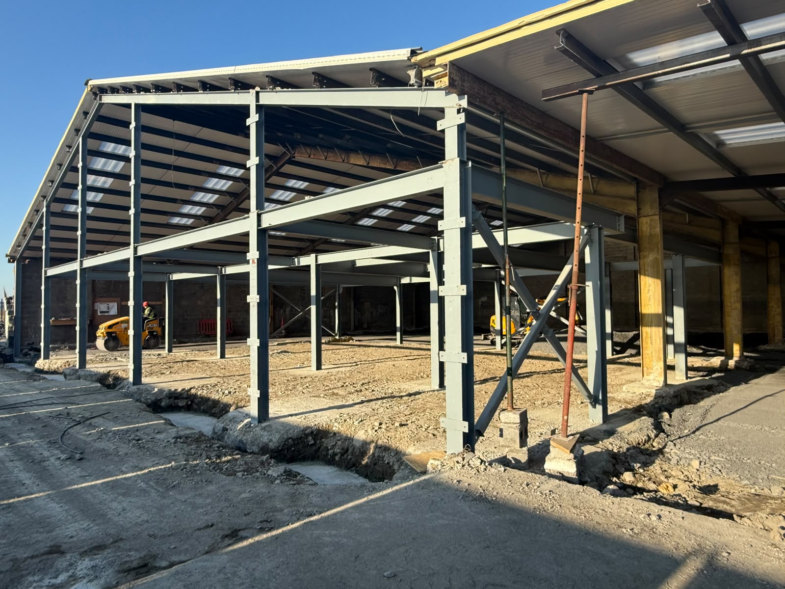 Grey painted steel portal frame extension with bracing erected alongside an existing building, with temporary props in place