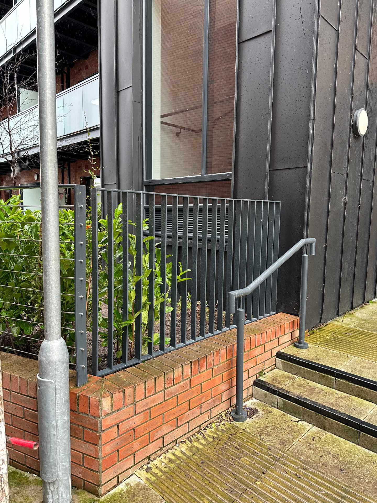 Dark grey vertical bar steel railings and a tubular handrail beside brick steps at an apartment entrance