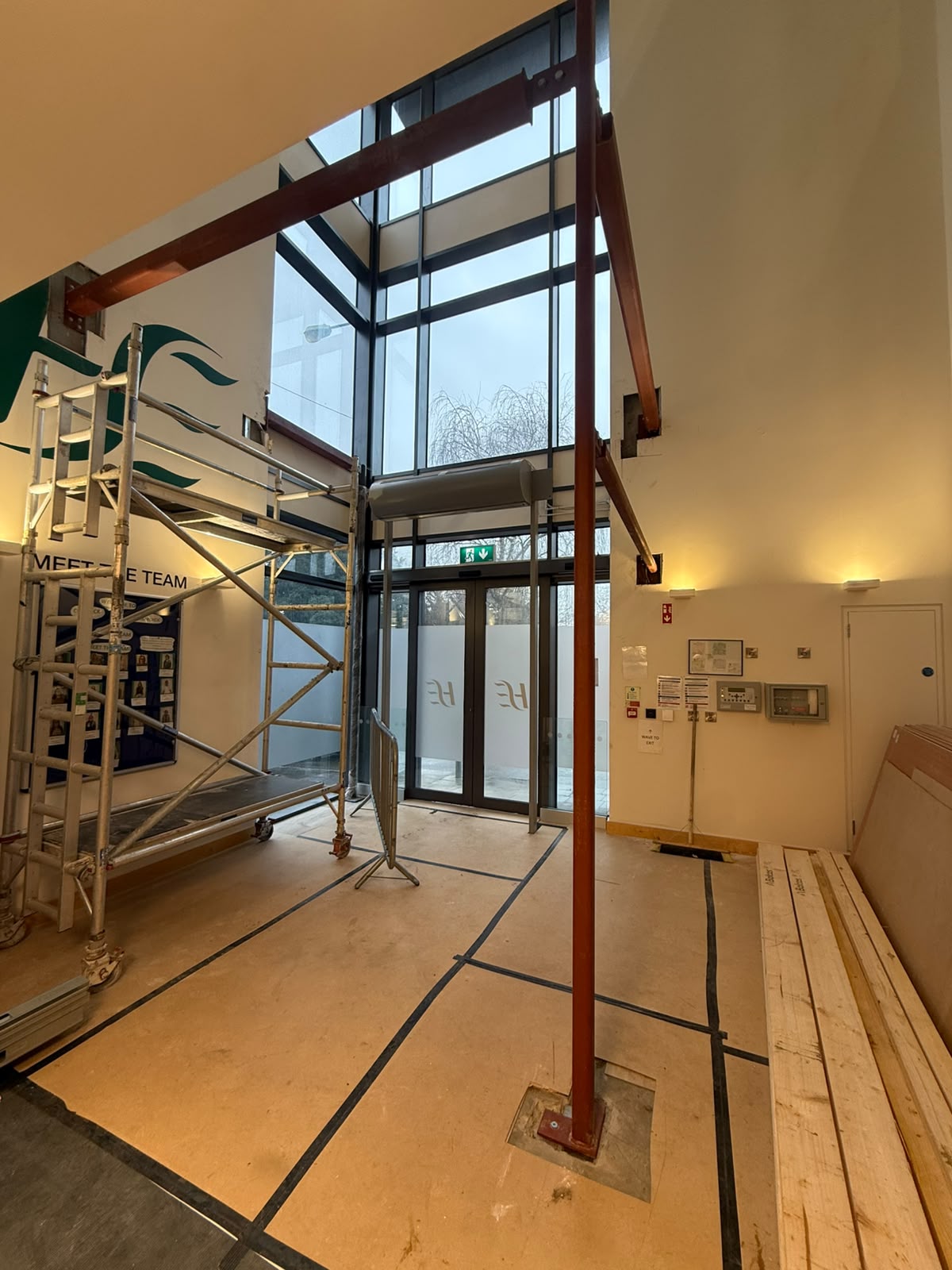 Red oxide painted steel goal post frame installed around a glazed double height office entrance during alterations