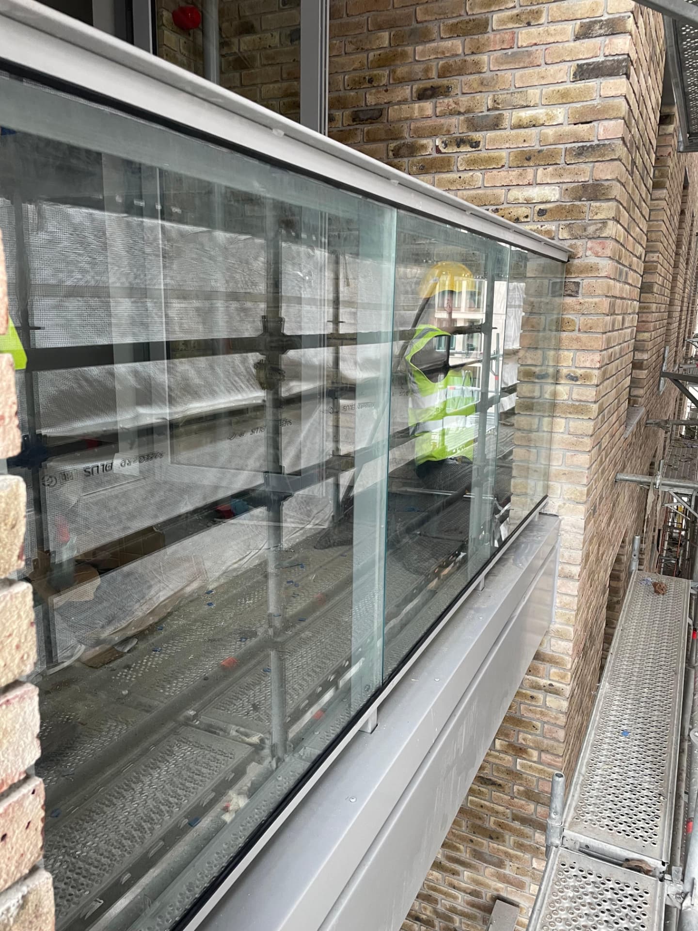 Close view of glass balustrade panels and capping rail on a balcony with brickwork alongside
