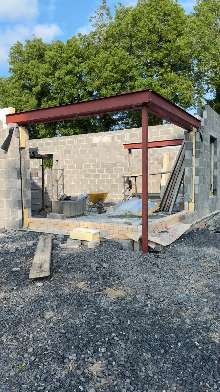 Red oxide steel beams and a corner column forming a flat roof frame over new blockwork walls of a house extension