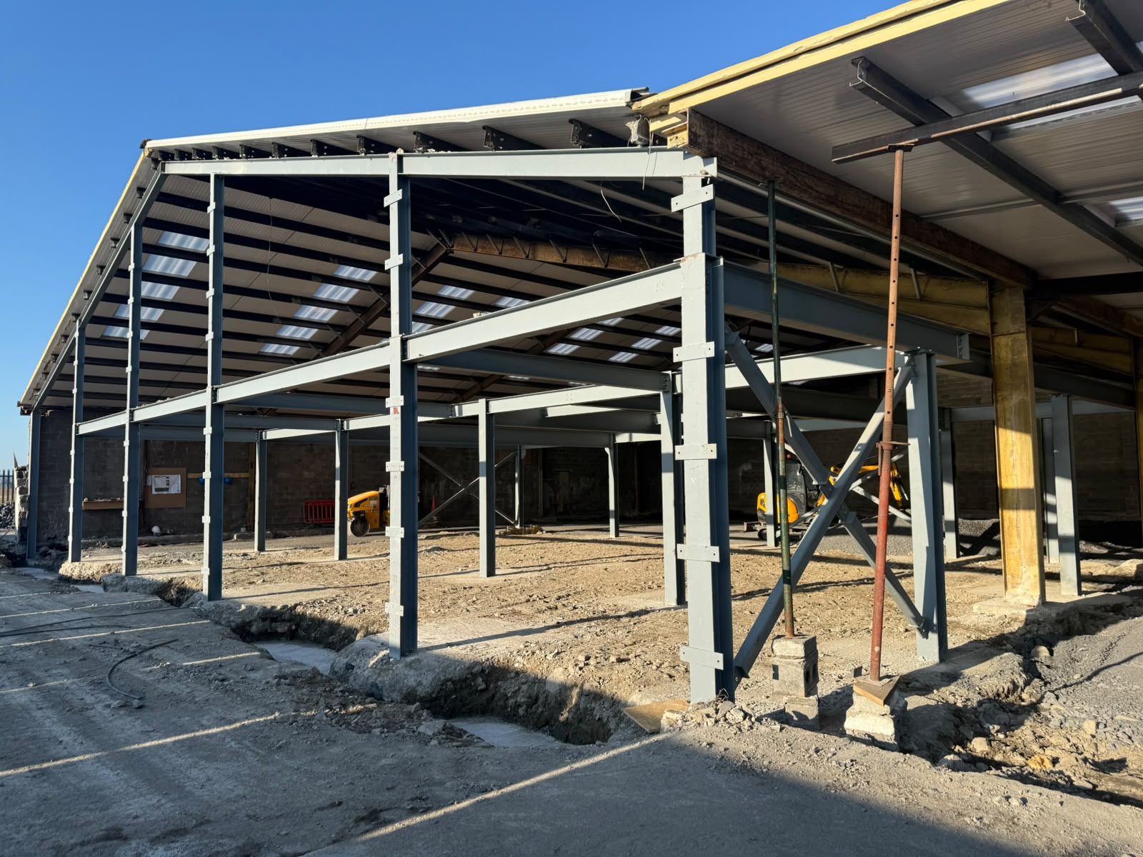 Side elevation of the grey steel extension frame with roof sheeting and bracing in place