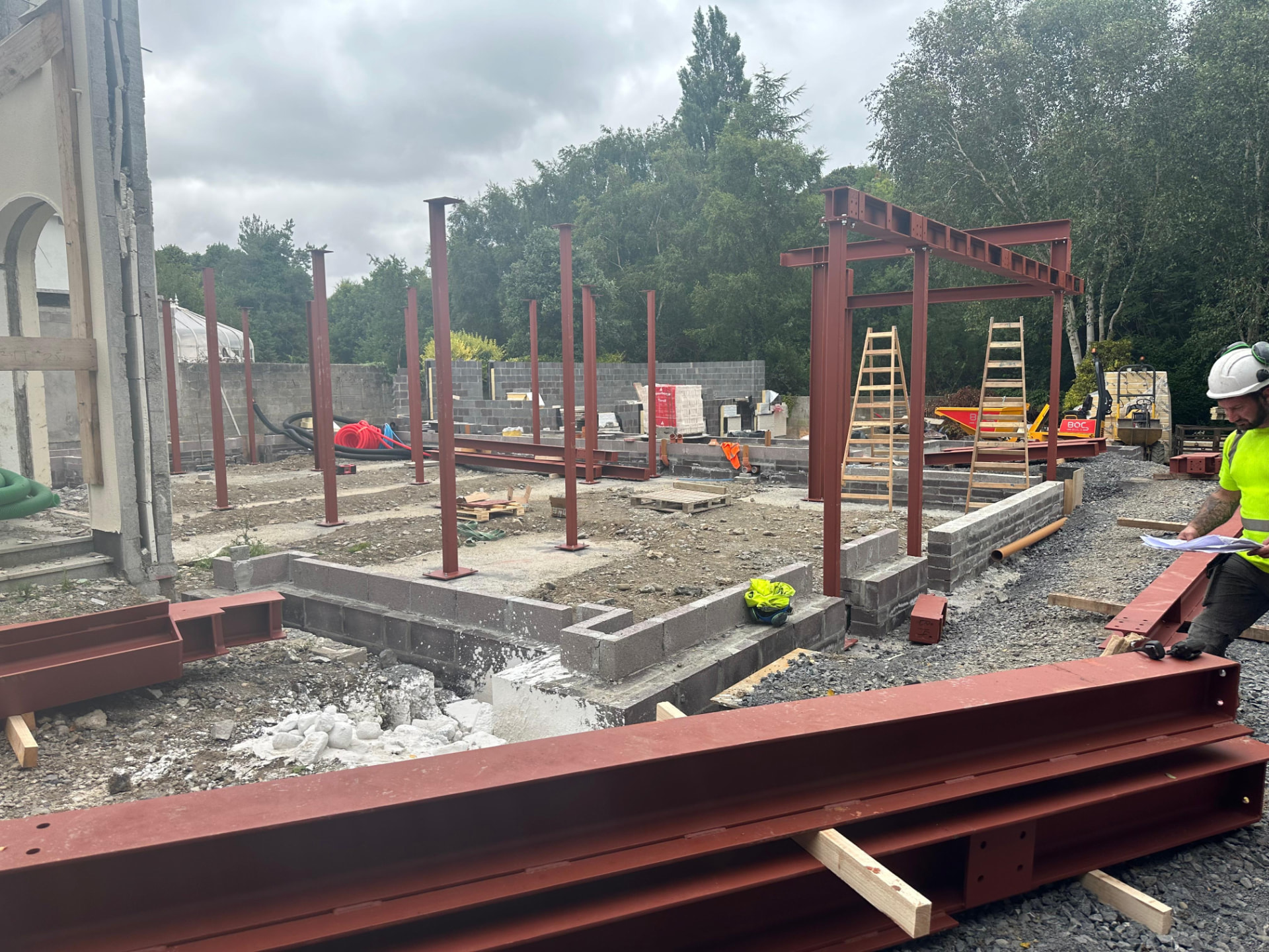 Red oxide painted steel columns set on pad foundations with beams laid out ready for erection on a new build site