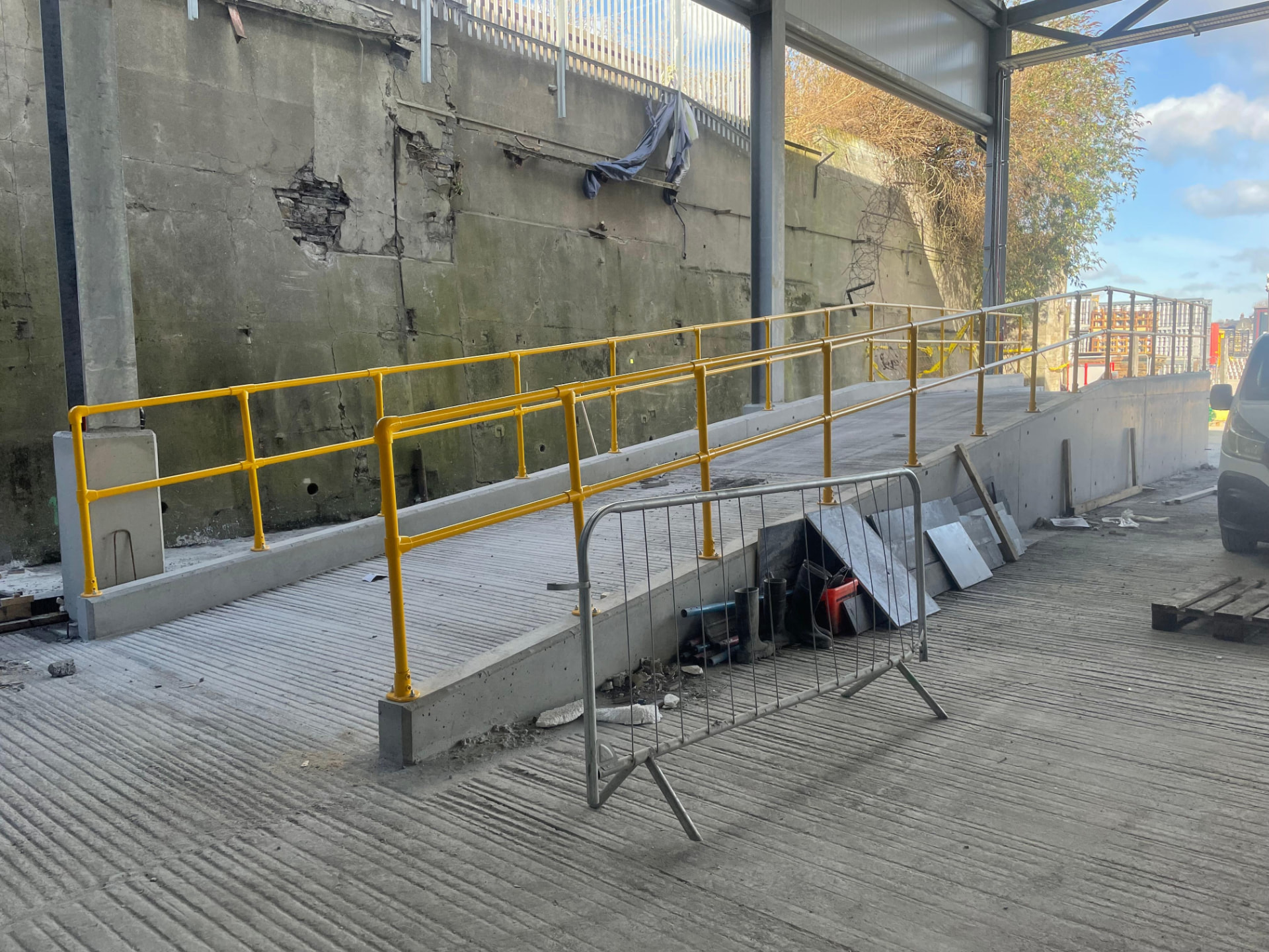 Yellow safety handrail following the pitch of a concrete access ramp inside a steel framed building