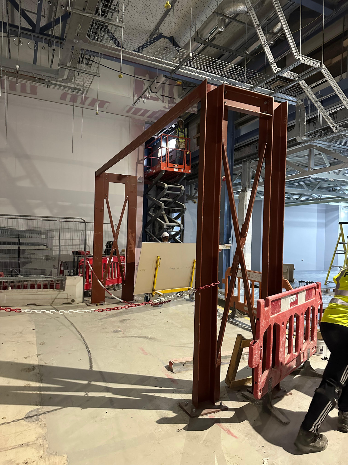 Red oxide painted steel goal post frame with cross bracing standing inside a commercial fit out with services overhead