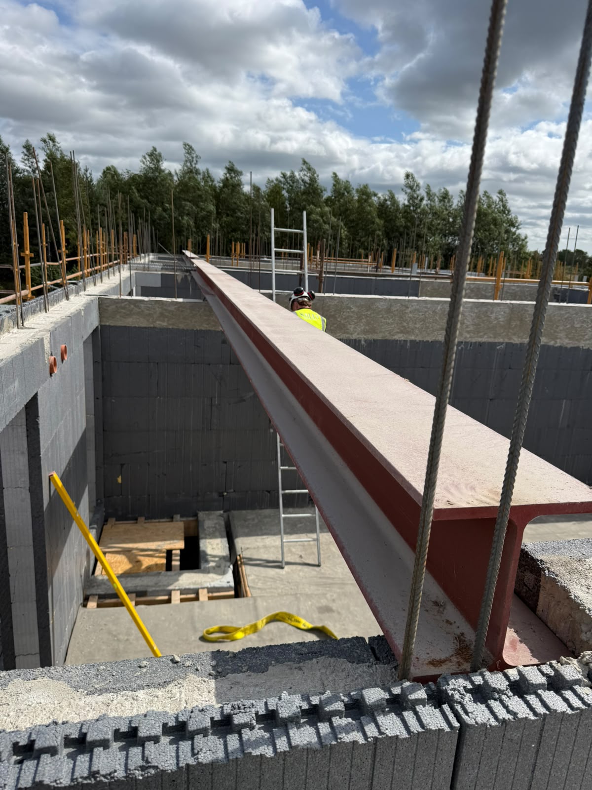 Long red oxide painted steel beam being craned into position across blockwork walls on a new build site