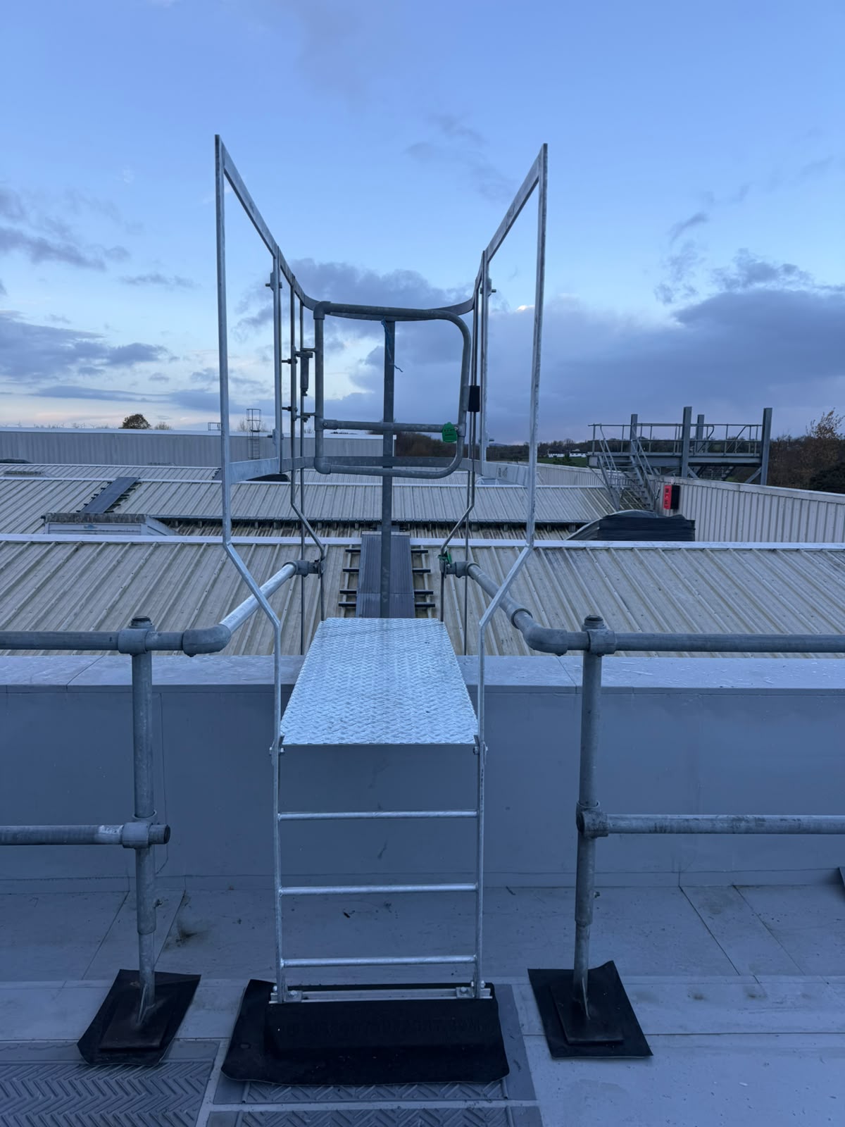 Galvanised roof access step over platform with chequer plate tread, side guarding and a self closing safety gate