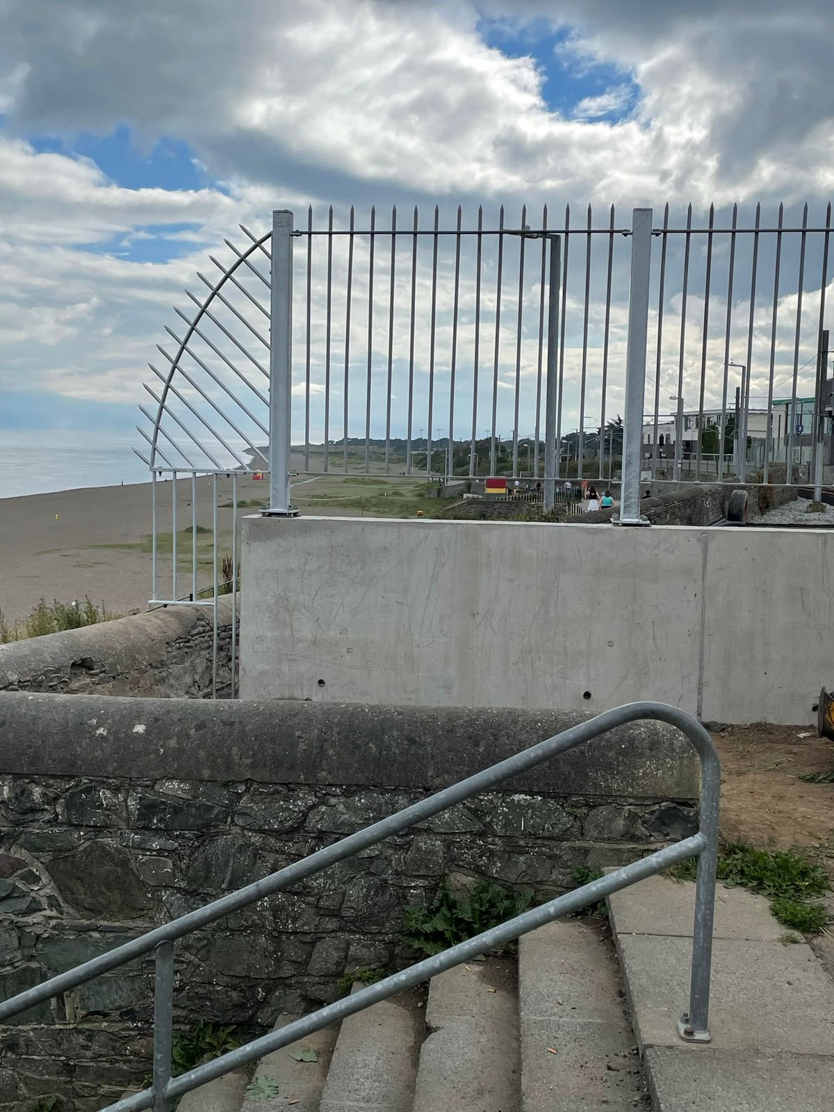 Galvanised vertical bar palisade railings with pointed tops on a coastal sea wall beside a stepped access with handrail