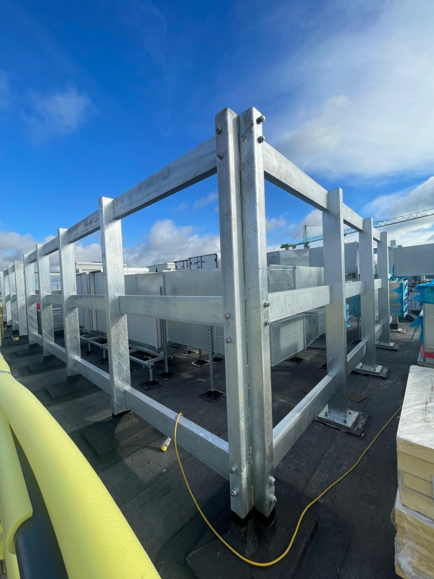 Galvanised steel frame with posts and rails enclosing rooftop plant and ductwork under a blue sky