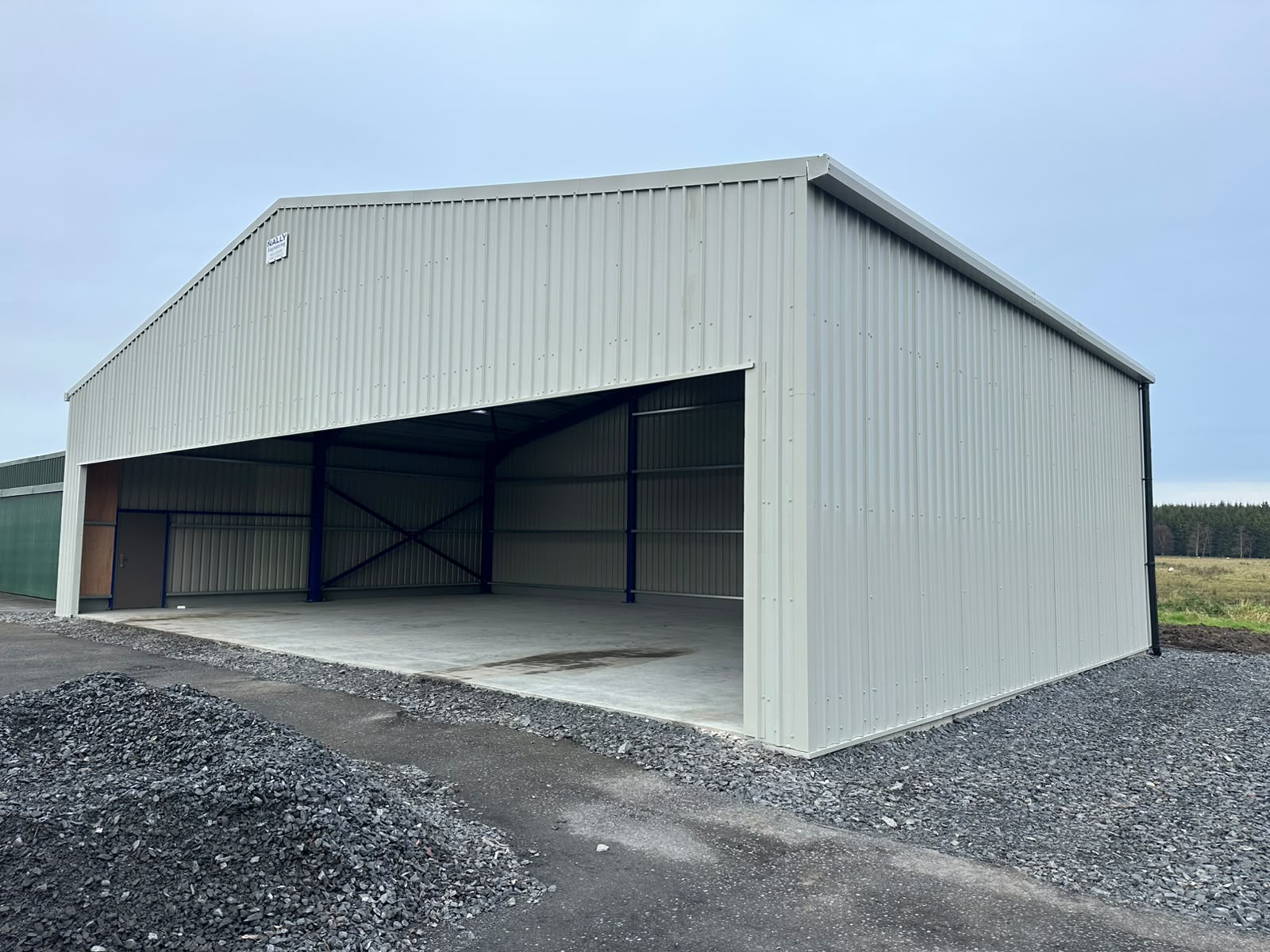 Pale grey clad steel shed with a full width open front bay, blue painted internal frame and new concrete floor