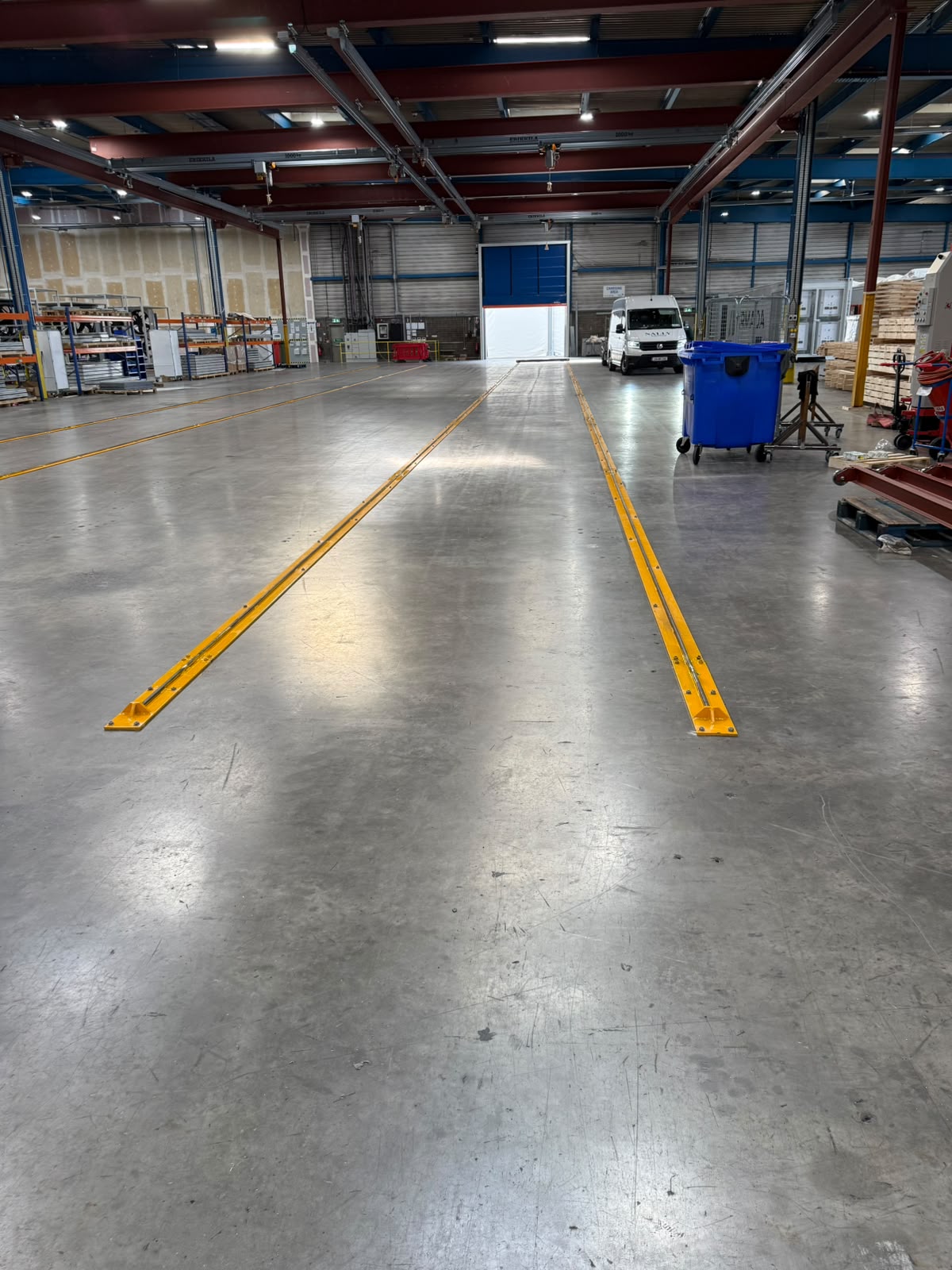 Yellow steel guide rails bolted into a factory floor running towards a blue loading door