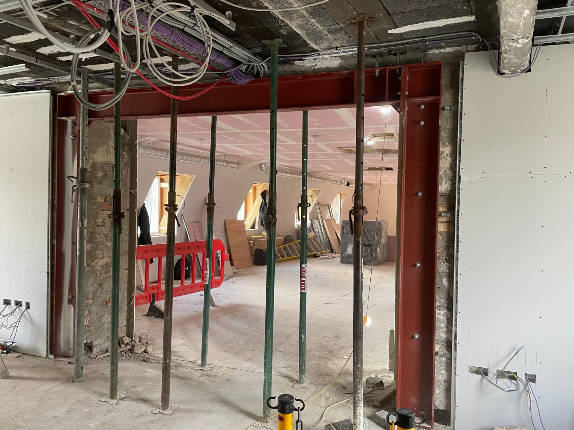 Red oxide steel beam and columns forming a wide internal opening with temporary acrow props still in place