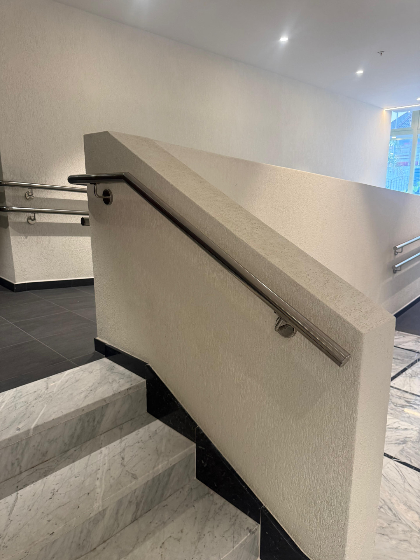 Stainless handrail following the rake of a rendered stair wall in a marble tiled lobby
