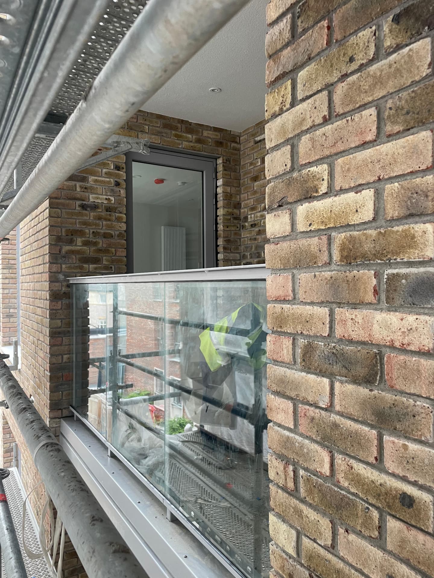 Frameless glass balustrade with a metal capping rail installed to an apartment balcony behind scaffolding