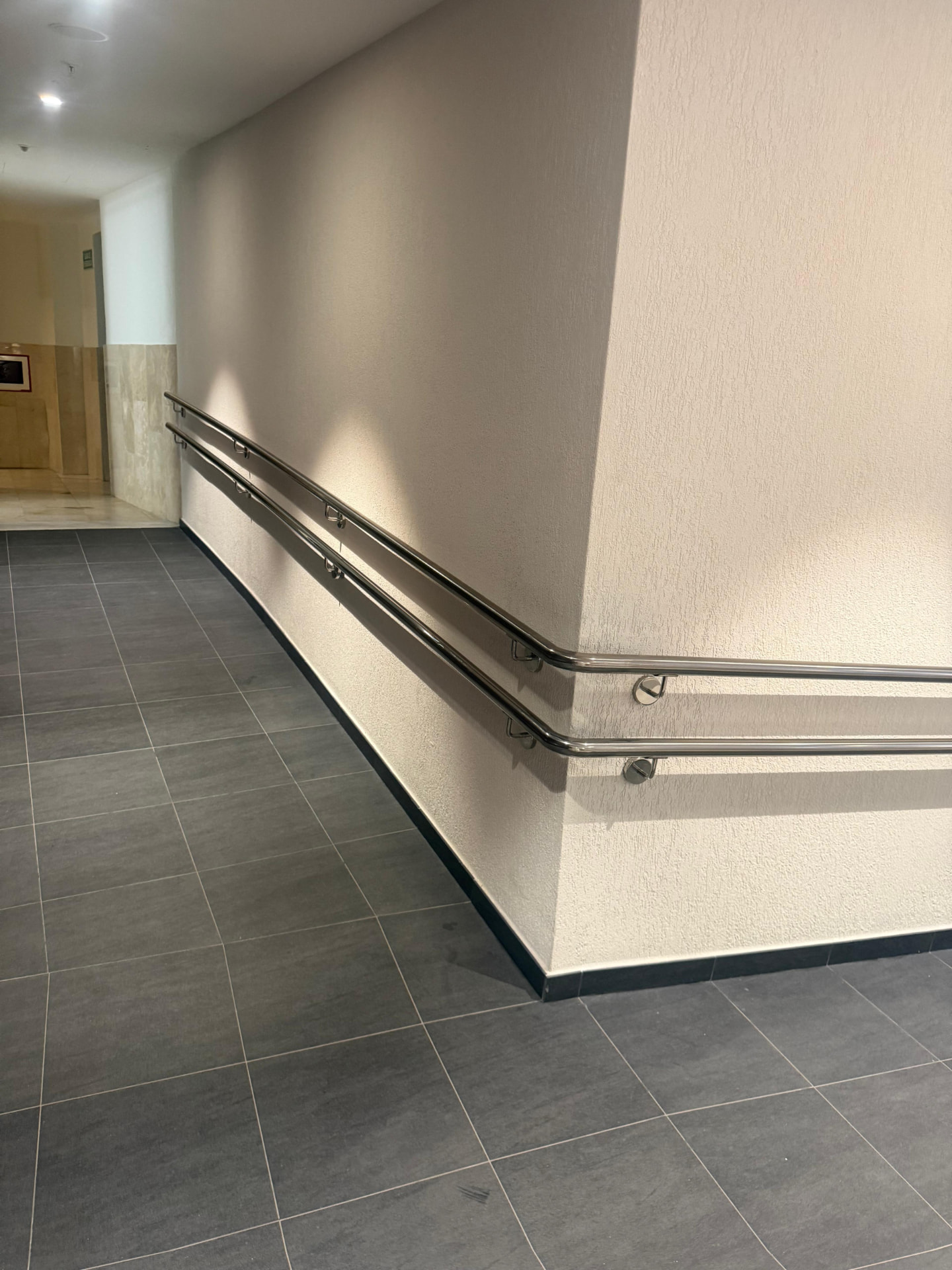 Long double stainless handrail run turning a corner in a tiled corridor