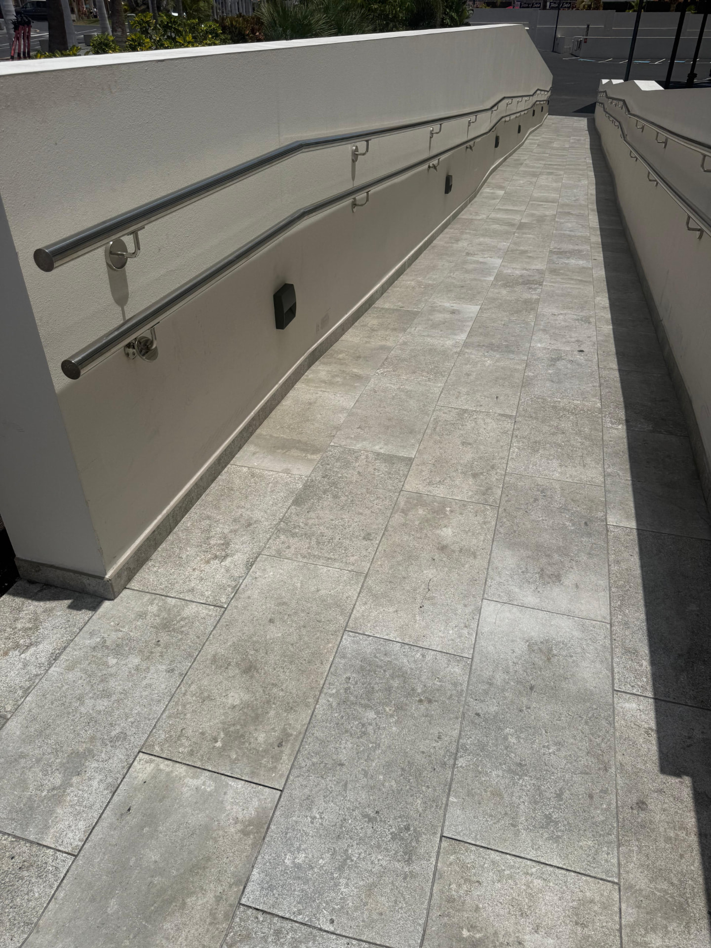 Double stainless handrails fixed to the rendered wall of an external tiled access ramp