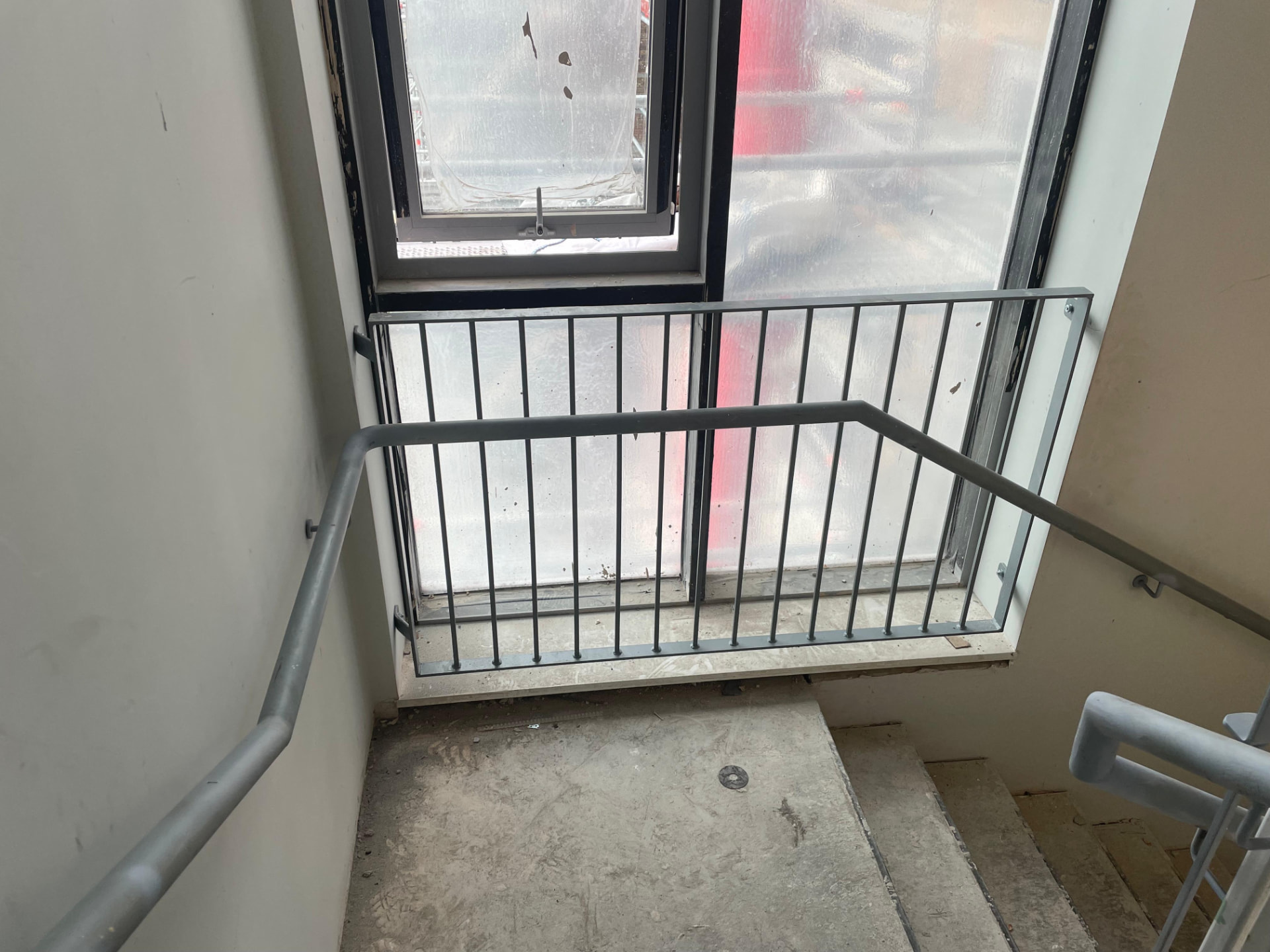 Grey steel balustrade with vertical bars and tubular wall handrails to a concrete stair landing