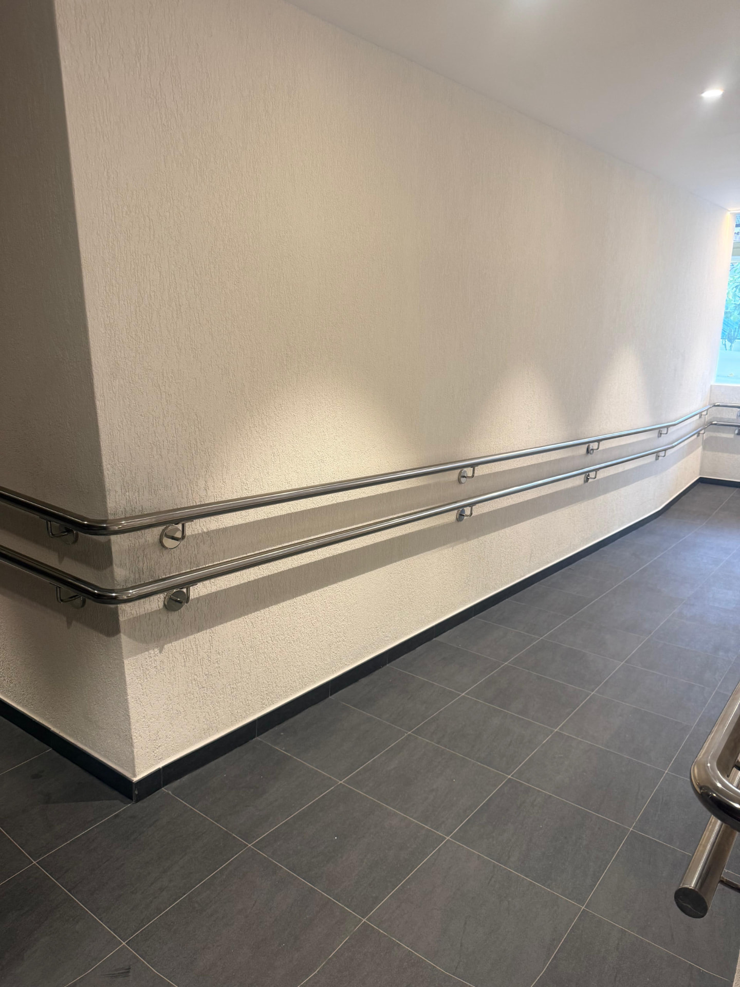 Two stainless handrails curving around a corner of a rendered corridor wall