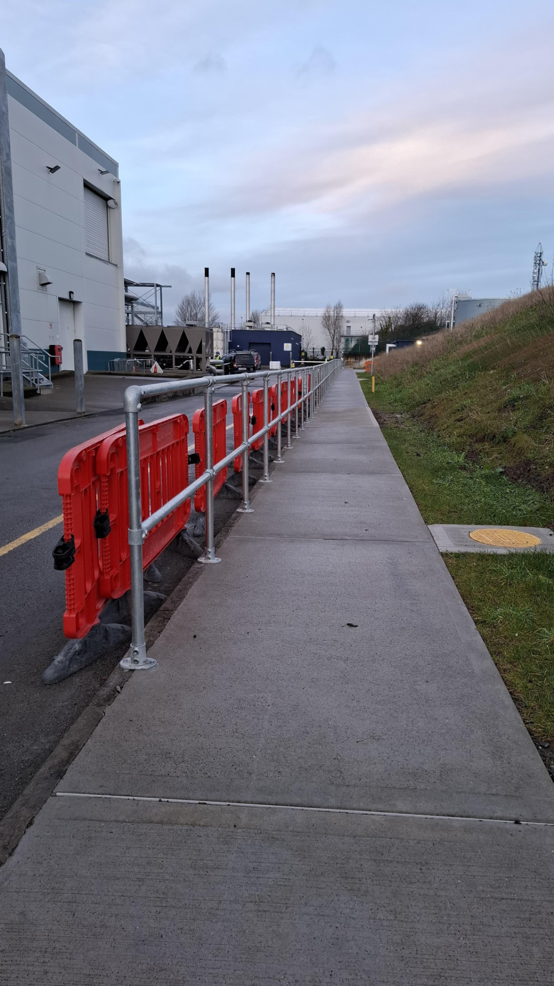 Galvanised tube guardrail running along the edge of a new concrete pedestrian walkway on an industrial site