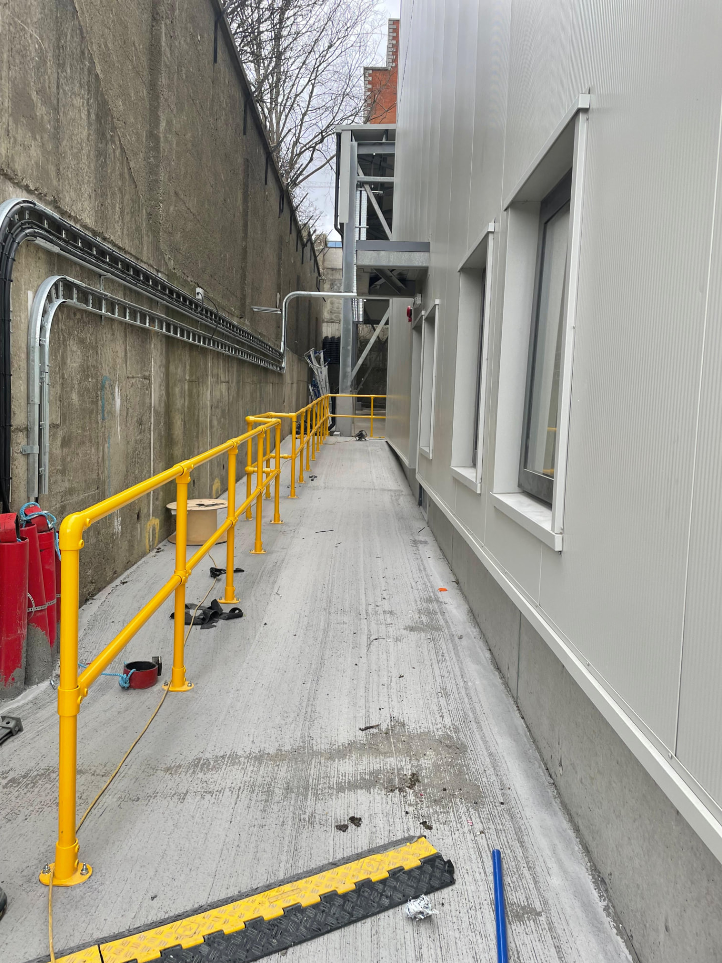 Bright yellow tubular safety handrail with base plated posts running along a narrow service walkway
