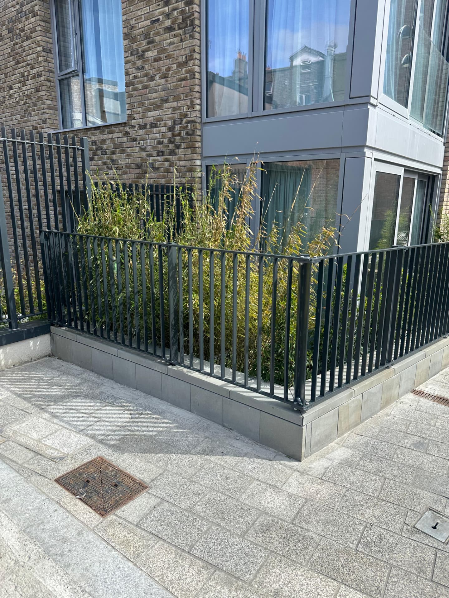 Dark grey vertical bar railings returning around a planted corner on a concrete plinth