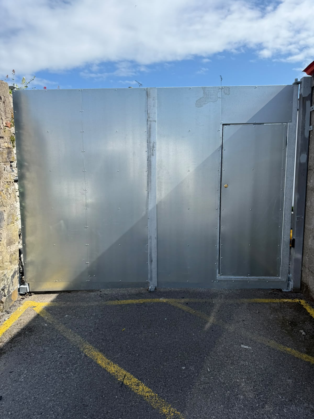 Galvanised sheeted sliding gate with a built in personnel door closing off a walled yard entrance