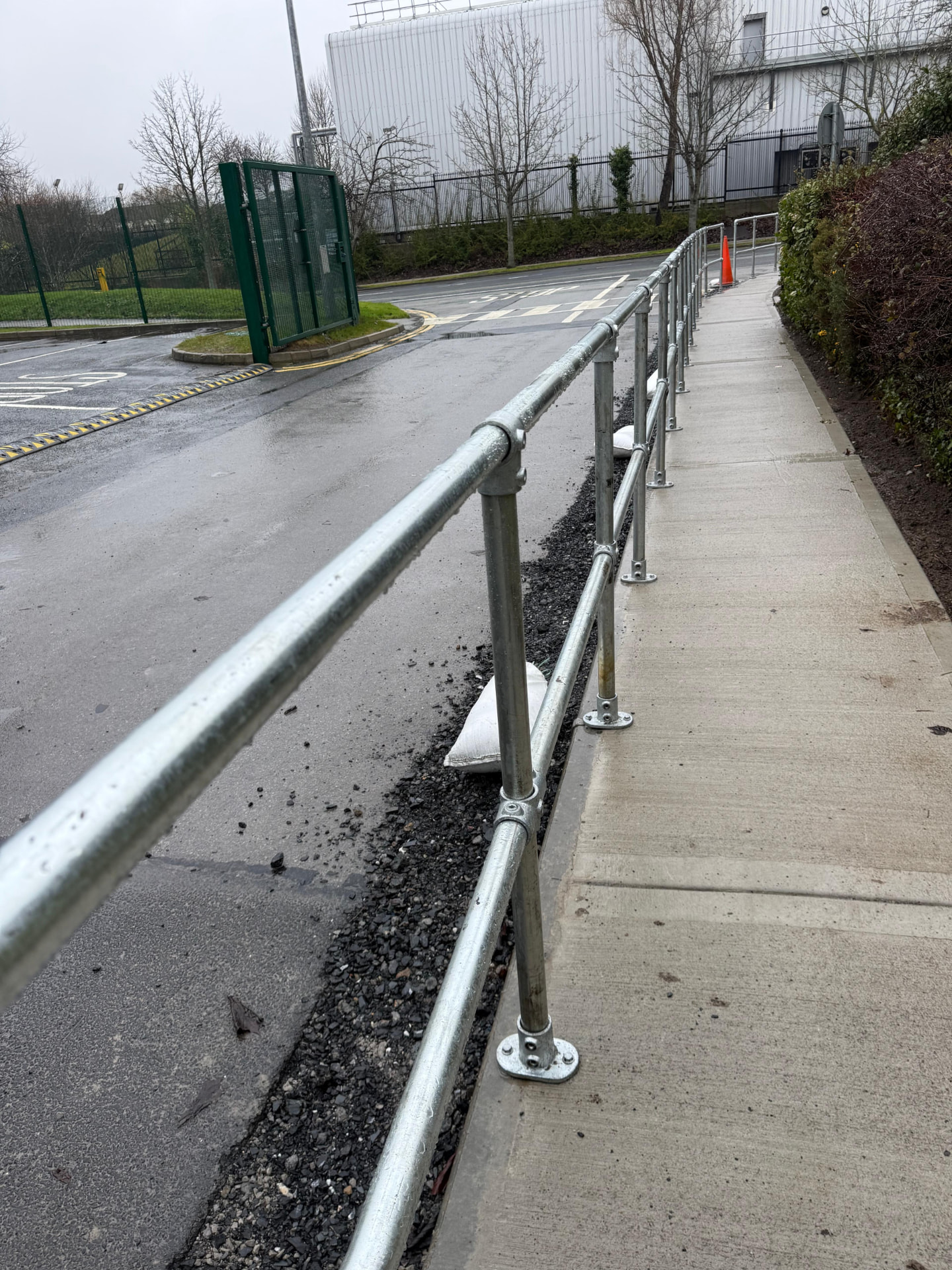 Galvanised tube guardrail with bolted base plates following the curve of a walkway beside a site road