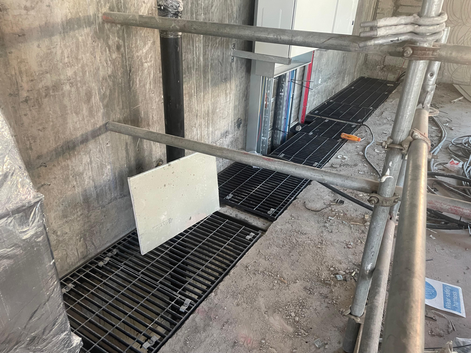 Black open mesh grating panels set into a concrete floor over a service riser inside a building under construction