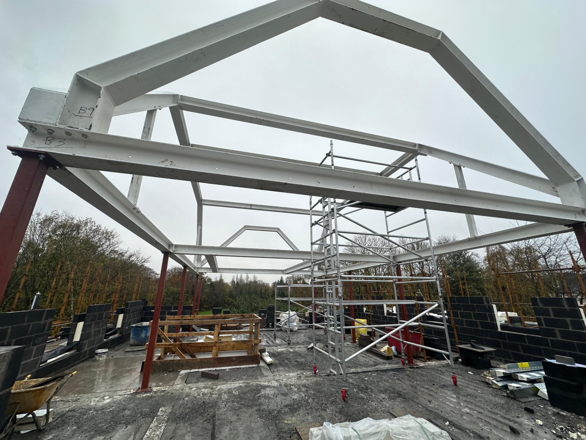 White painted apex steel portal frame with rafters and ties erected on red columns above new blockwork walls